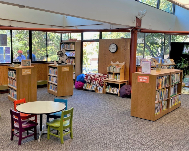 A view of the interior of the Corte Madera library branch showing shelves, books, a table and chairs.