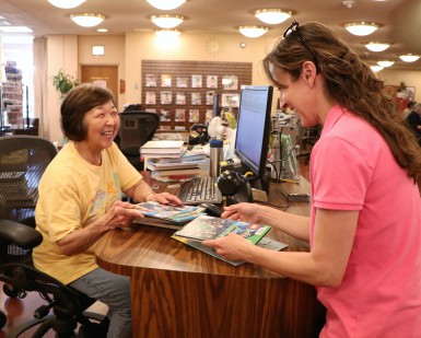 A librarian smiles at a female patron checking out books.