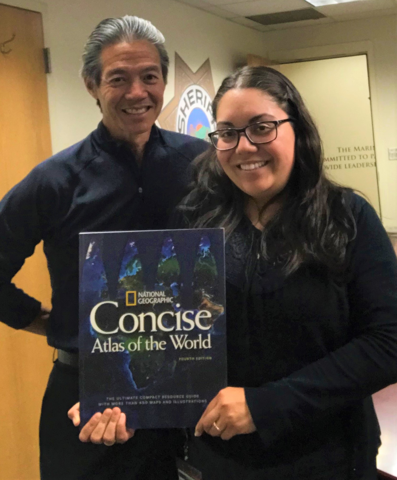 America Velasco from the jail staff holds up a world atlas as librarian Elmer Jan stands behind her.