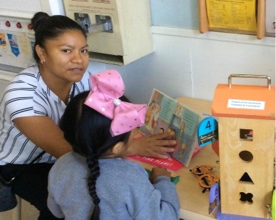 A mother reads a book to a young girl at the small library inside a laundromat.