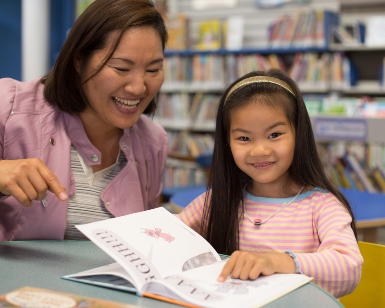 A mother and daughter of about 5 years old read a book together at a library.