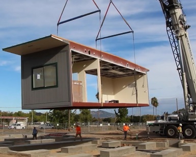 A large crane hoists a modular building into place at the new site of the South Novato Library.