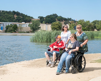 Two women standing behind two other people in wheelchairs at the edge of Lagoon Park at the Marin County Civic Center.