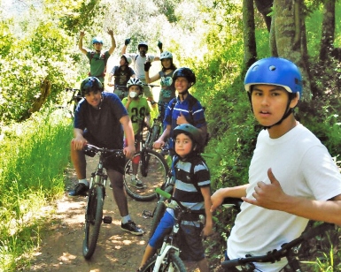 A group of young boys pause on a trail with their mountain bikes and wave to the camera.