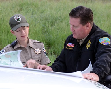 A parks ranger talks to a Sheriff's deputy in the parking lot of a County open space area.