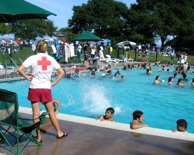 A female lifeguard stands watch next to the McNears Beach Park pool as kids play in the water.