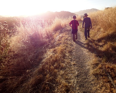 Two young boys walk on an unpaved path toward the sunset