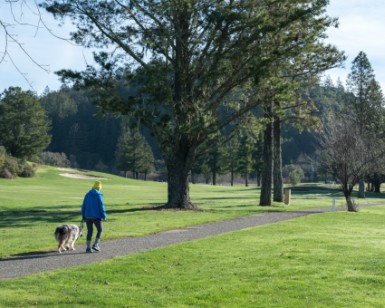 A person walks a dog on a paved path at San Geronimo Golf Course.