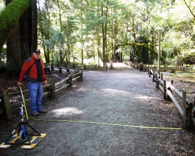 A surveyor measures the width of a trail in the forest.