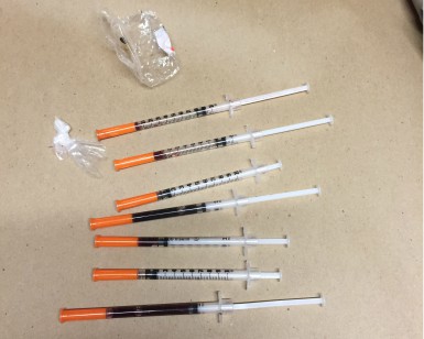 A collection of seven hypodermic needles and suspected drugs on a table.