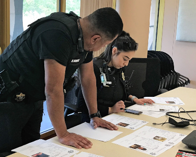 Two Probation Department officers, one female seated a table and one male standing and leaning on the table, look at printed documents before a DUI compliance check.