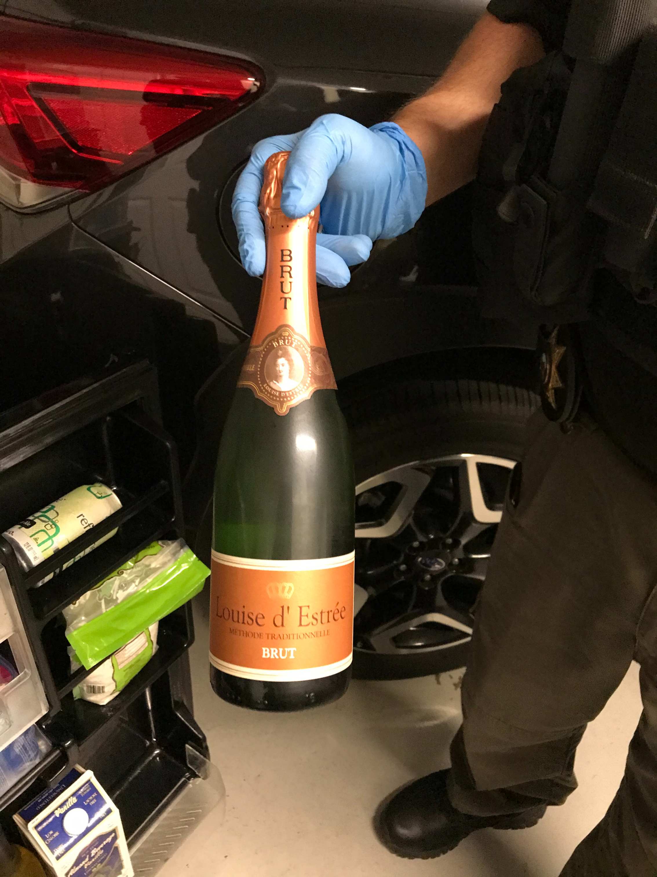 The gloved hand of a probation officer holds up a bottle of sparkling wine confiscated during a DUI compliance check.