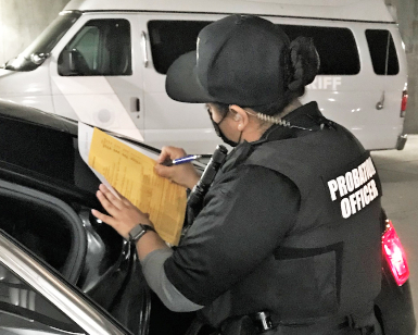 A probation officer fills out a form while leaning on the roof of a probation vehicle.