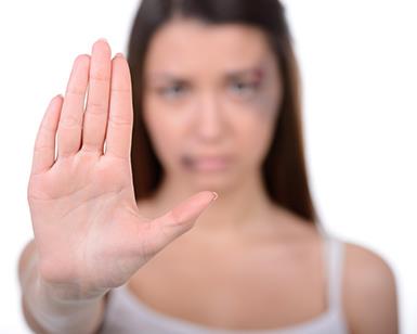 A woman with facial bruises holds up her hand as if to say "stop"