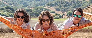 Three women smiling in an orange hammock 