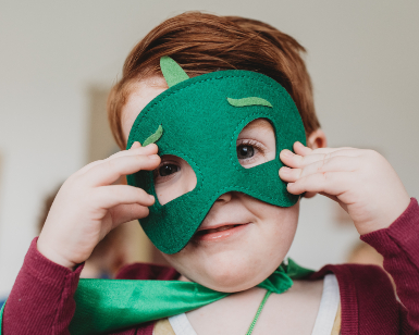 A young smiling boy adjusts his homemade green felt mask 